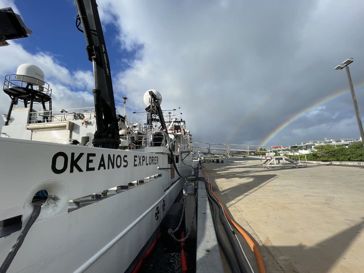 NOAA Ship Okeanos Explorer alongside a pier, a rainbow visible in the distance